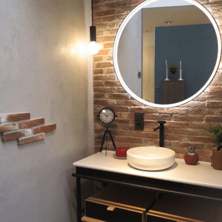 Bild mit einer schönen Raumecke. Auf der linken Seite eine weiße Wand und auf der rechten Seite ein runder Badspiegel mit Pflasterstein-Wand und Waschbecken.