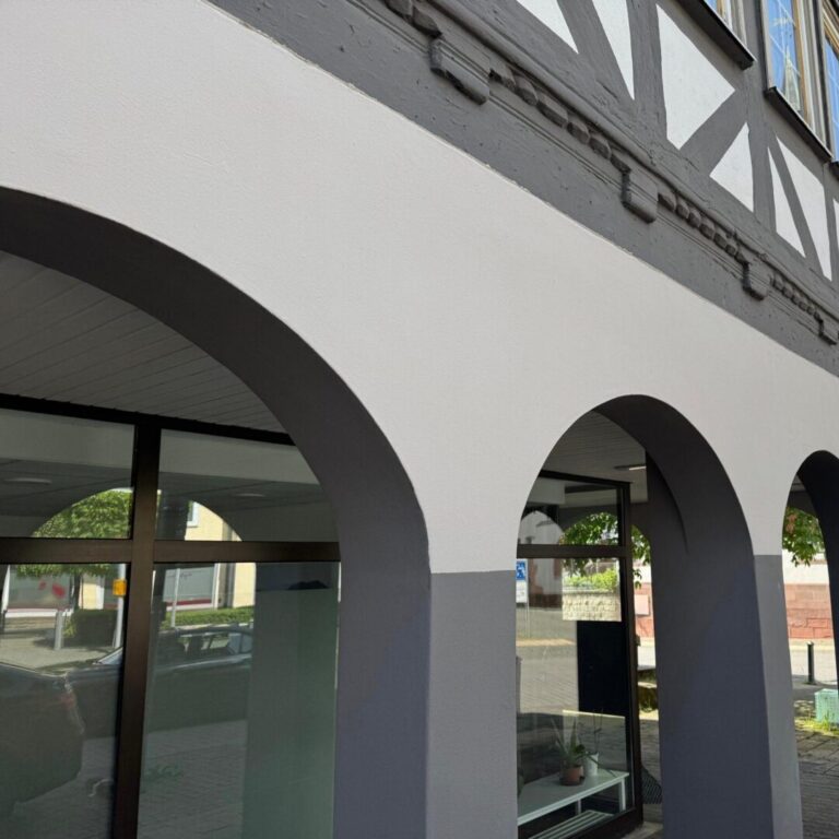 Näheres Bild der Fachwerkhaus-Fassade gestrichen in weiß-anthrazit. Eine Bogenstruktur mit Pfeilern.