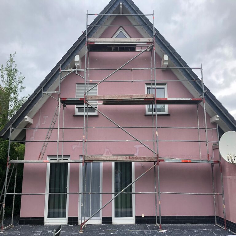 Hausfassade gestrichen in Pink mit Gerüst vor dem Haus